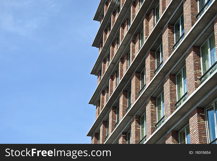 Fragment of the facade of the modern brick residential house with the same balcony. Detail. Against the blue sky.