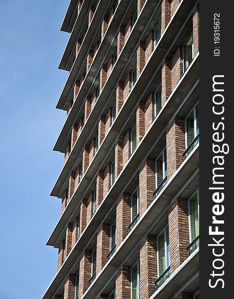 Fragment of the facade of the modern brick residential house with the same balcony. Detail. Against the blue sky.