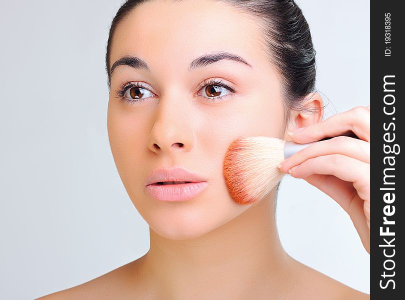 Beautiful woman applying make-up with brush