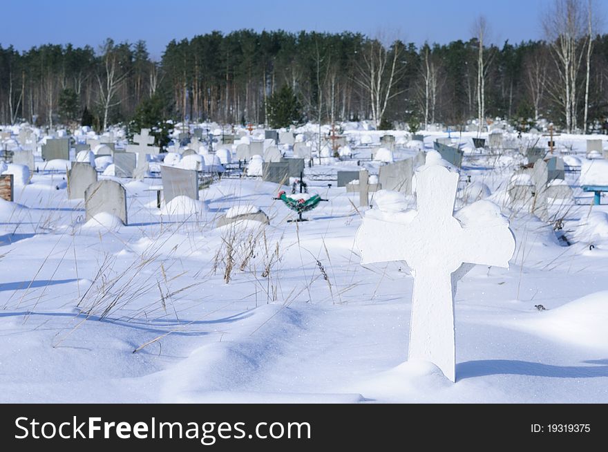 View of the snow-covered cemetery with a cross in the foreground. View of the snow-covered cemetery with a cross in the foreground