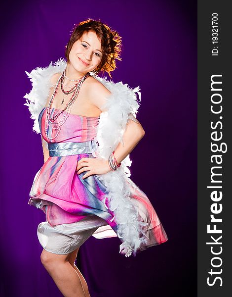 Beautiful girl with pink dress and white boa posing on purple background