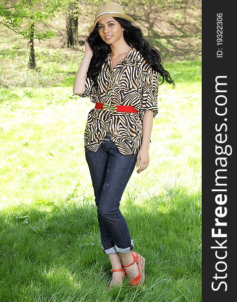 Cute brunette woman with hat smiling in the park. Wears an animal print blouse.