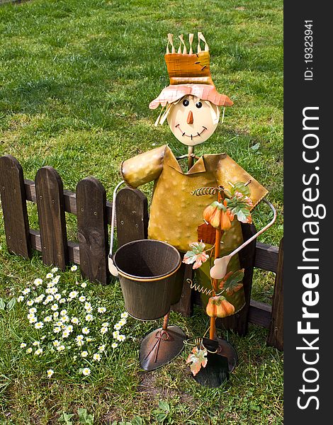 A metal scarecrow in the garden with a wooden fence in the background