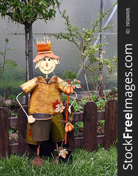 A metal scarecrow in the garden with a greenhouse in the background