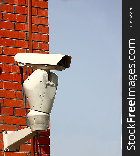 A surveillance, security camera on a brick wall and blue sky background. A surveillance, security camera on a brick wall and blue sky background
