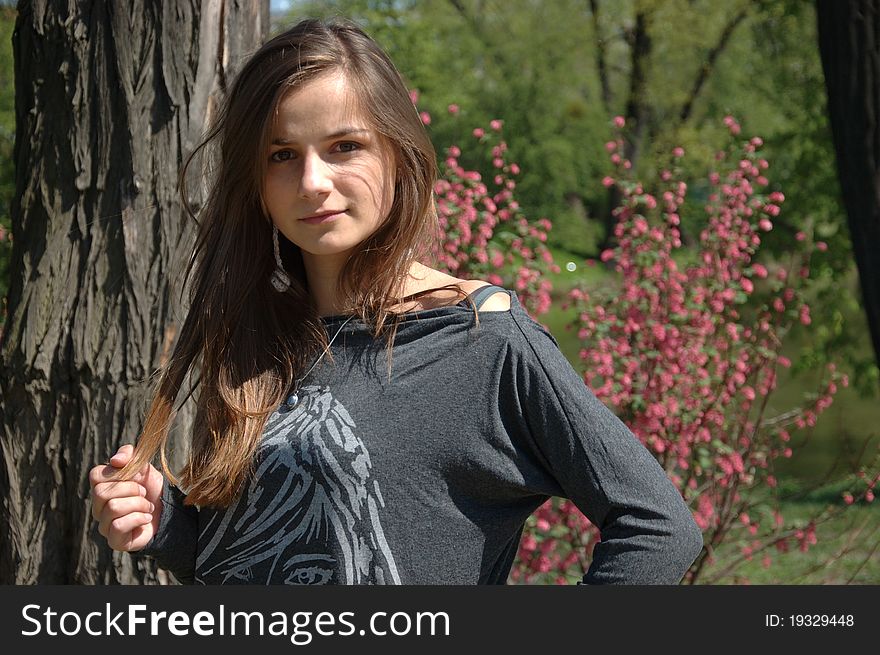 Young girl in park. Polish model wearing casual clothes, holding her hairs. Posing in park with trees as background. Young girl in park. Polish model wearing casual clothes, holding her hairs. Posing in park with trees as background.