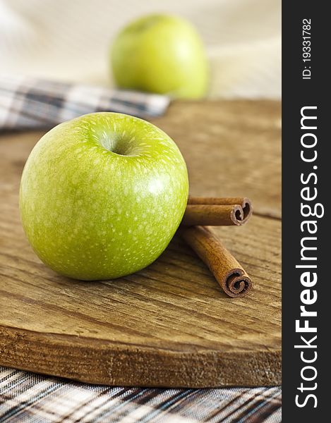 Green apple and cinnamon sticks on wooden board