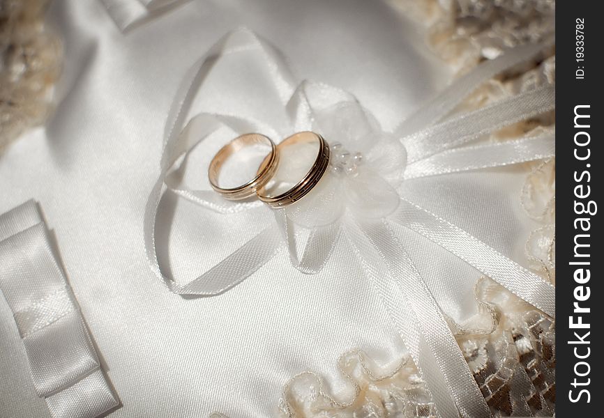 Pair of gold wedding rings on a white wedding pillow