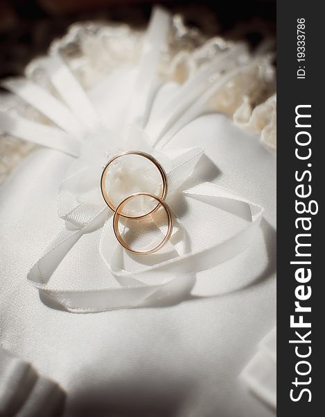 Pair of gold wedding rings on a white wedding pillow