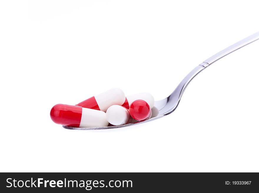 Several colored capsules on a spoon with white background