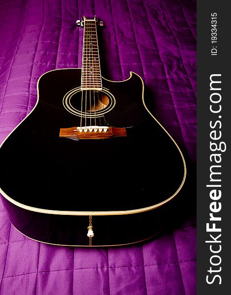 Black shiny acoustic guitar on bed. Black shiny acoustic guitar on bed