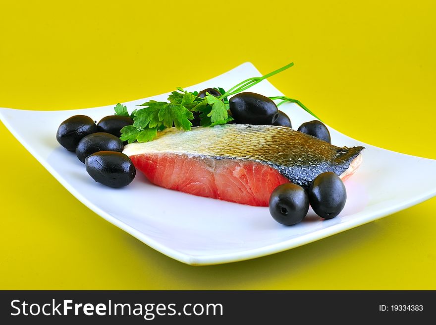 Part of salted fish salmon lying on a white plate beside large black olives. Part of salted fish salmon lying on a white plate beside large black olives