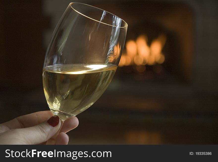 A glass of white wine by a lit fireplace. A glass of white wine by a lit fireplace.