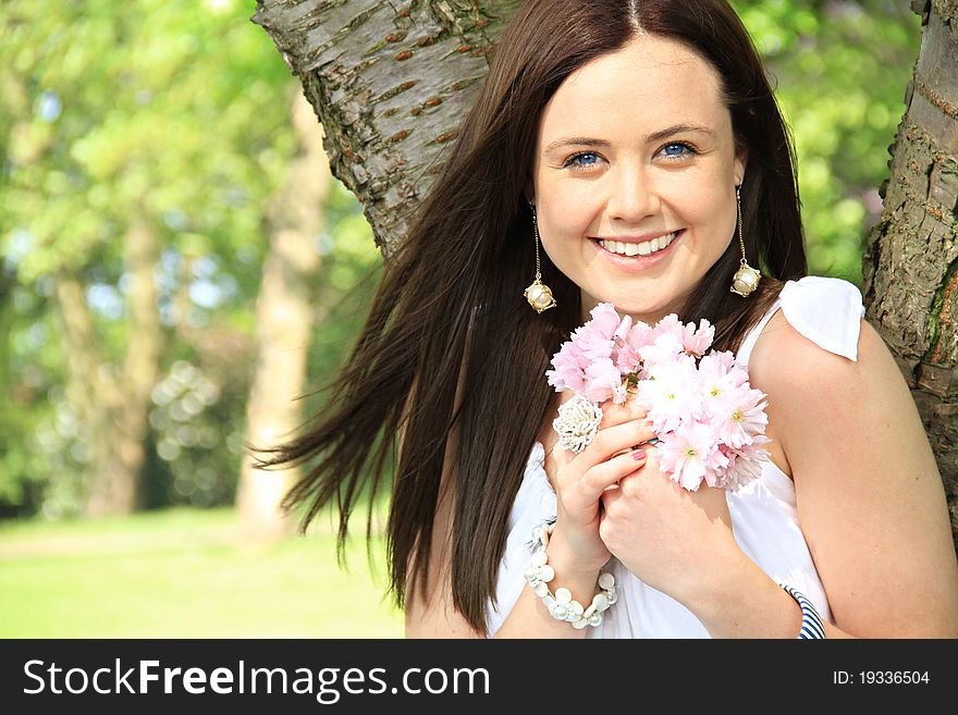 A happy woman holds and small bunch of flower close to her as she is enjoying a summers day.