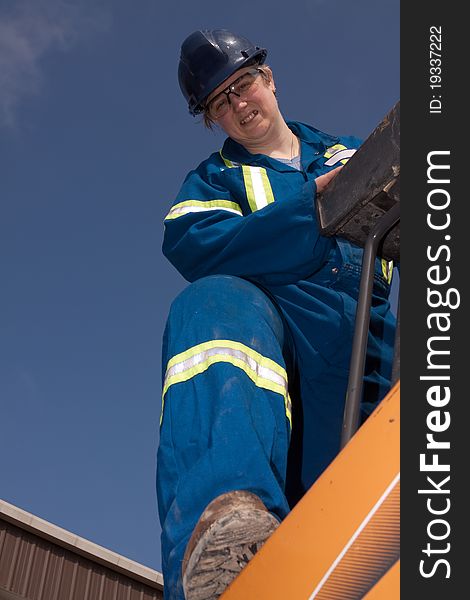 Portrait of a caucasian forties woman wearing coveralls and blue hard hat standing on tractor with blue sky in back. Portrait of a caucasian forties woman wearing coveralls and blue hard hat standing on tractor with blue sky in back