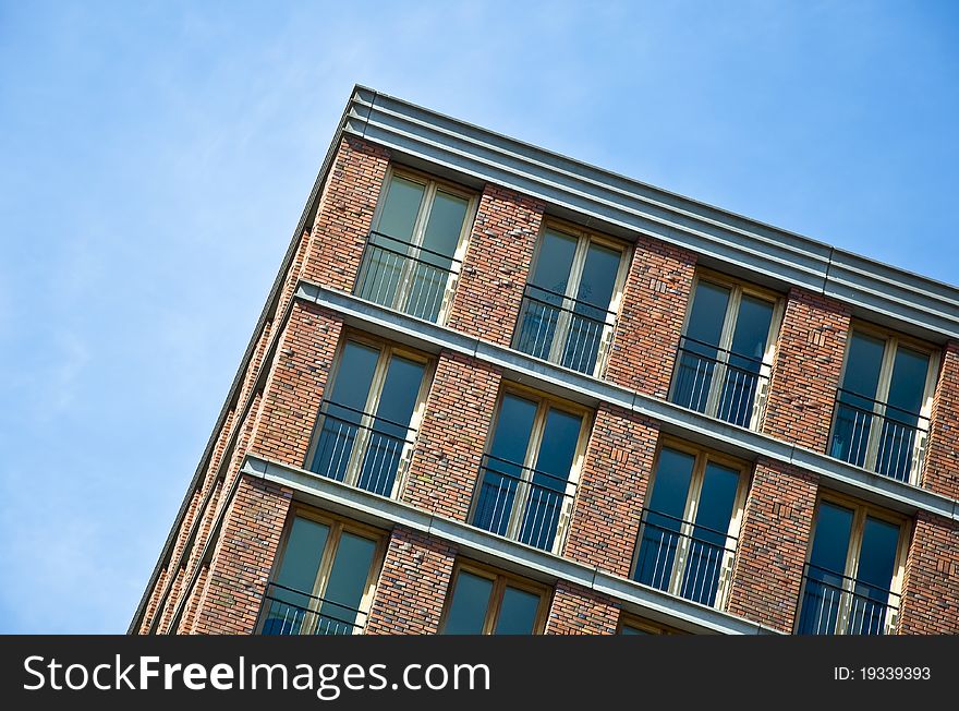 Fragment of the facade of the modern brick residential house with the same balcony. Detail. Against the blue sky.