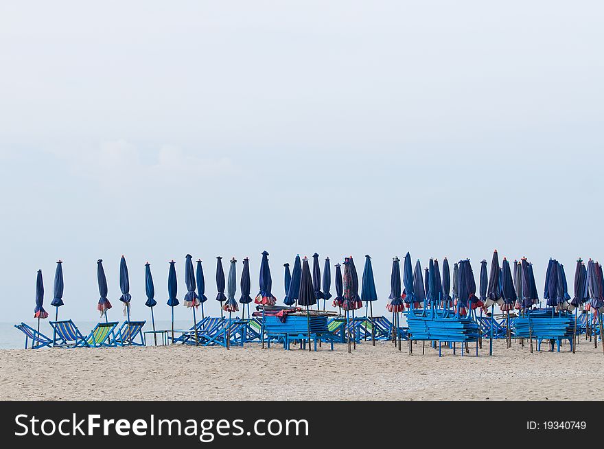 Empty, wooden beach chairs and folded parasols at the beach. Empty, wooden beach chairs and folded parasols at the beach.