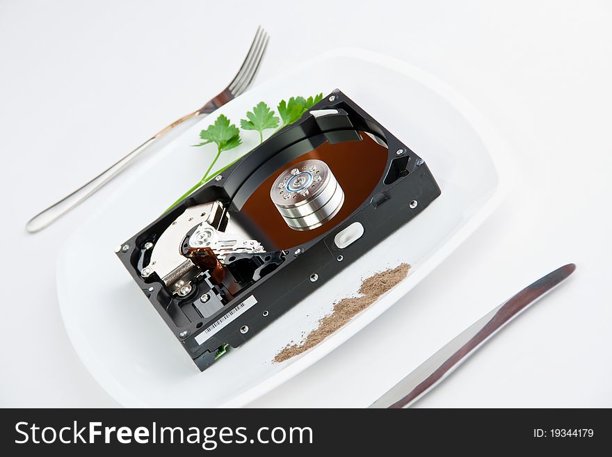 Hard drive on the dining plate with seasoning and herbs surrounded by a knife and fork. Hard drive on the dining plate with seasoning and herbs surrounded by a knife and fork