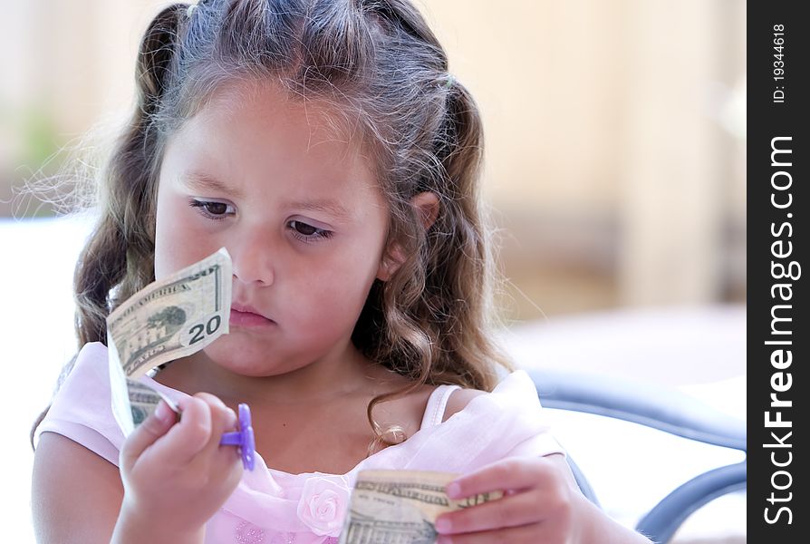 A young girl wearing pink party dress holding US Twenty dollar bill looking at it with concern expression. A young girl wearing pink party dress holding US Twenty dollar bill looking at it with concern expression.