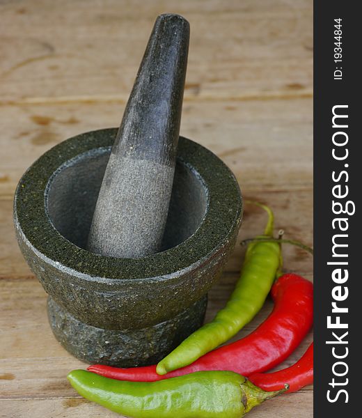 Stone mortar and pestle with chili on wood background