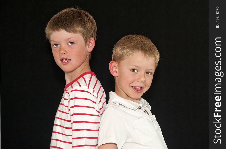 Two Adorable young brothers standing back to back isolated on a black background