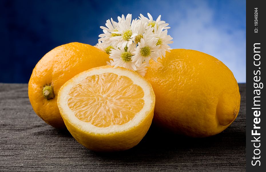 Photo of delicious yellow lemon fruit with marguerite on blue background