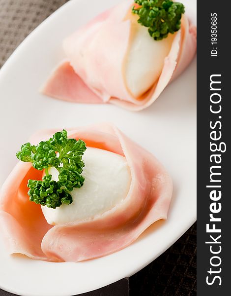 Photo of delicious mozzarella with wrapped ham on wooden table