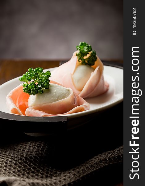 Photo of delicious mozzarella with wrapped ham on wooden table