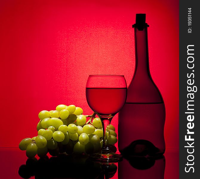 Wine composition (glass, bottle, grapes on red background)