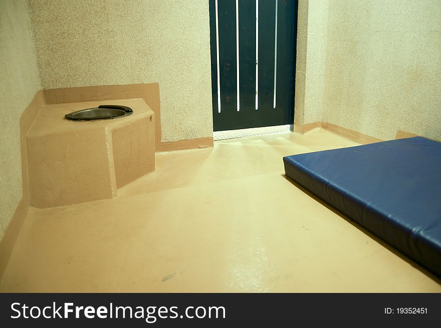 A naked prison cell with a mattres and a toilet