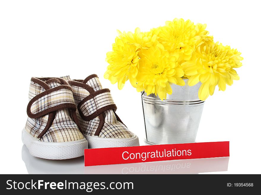 Little children's shoes near a bucket with flowers of yellow chrysanthemums. Isolated on white background. Little children's shoes near a bucket with flowers of yellow chrysanthemums. Isolated on white background