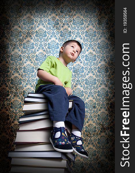 Small boy sitting on books. Nice dirty vintage wallpaper in background. This background is also available in the gallery