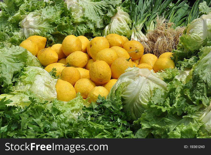 Fresh, moist yellow lemons surrounded by green salad ingredients lettuces, parsley, and green onions with roots all healthy low glycemic index foods. Fresh, moist yellow lemons surrounded by green salad ingredients lettuces, parsley, and green onions with roots all healthy low glycemic index foods.