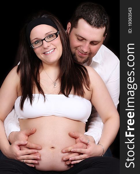 Happy expectng couple sitting with hands on her bare belly. Happy expectng couple sitting with hands on her bare belly