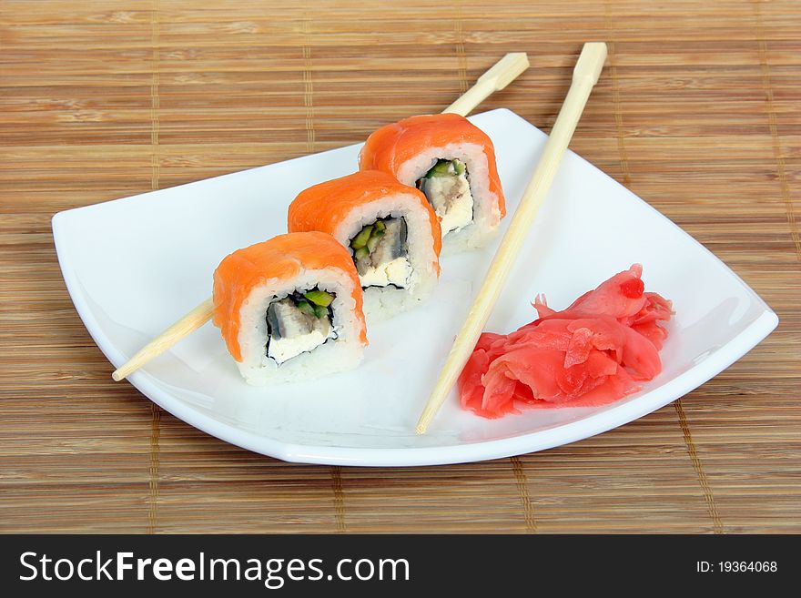 Close up of the three rolled salmon with conger, cucumber and ginger and two chopsticks on the white plate on the bamboo napkin background. Close up of the three rolled salmon with conger, cucumber and ginger and two chopsticks on the white plate on the bamboo napkin background.