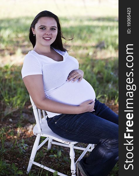 Pregnant woman sitting outside wearing jeans and t-shirt.