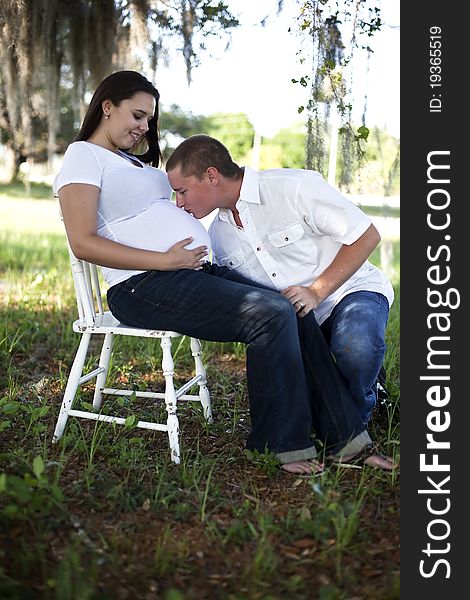 A young man kissing the belly of a pregnant young woman outdoors. A young man kissing the belly of a pregnant young woman outdoors.