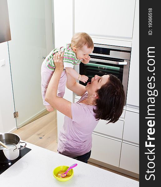 Young mother playing with her baby daughter in a modern kitchen setting. Young mother playing with her baby daughter in a modern kitchen setting.