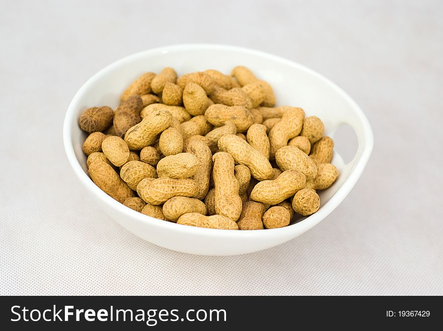 Pile of ripe crude peanuts in white bowl.