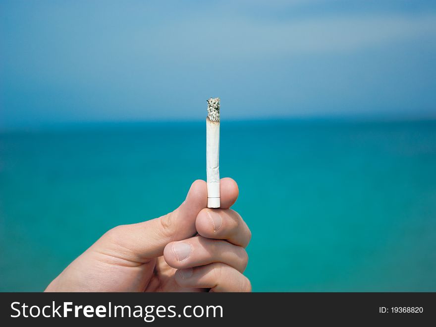 Hand holds a cigarette in the background of the sea