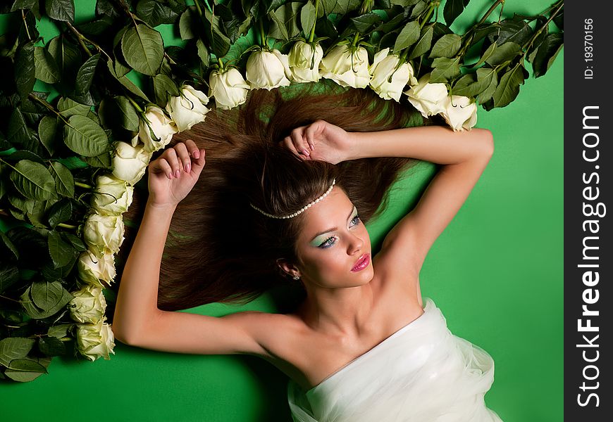 Young girl lay among the flowers of roses on a green background