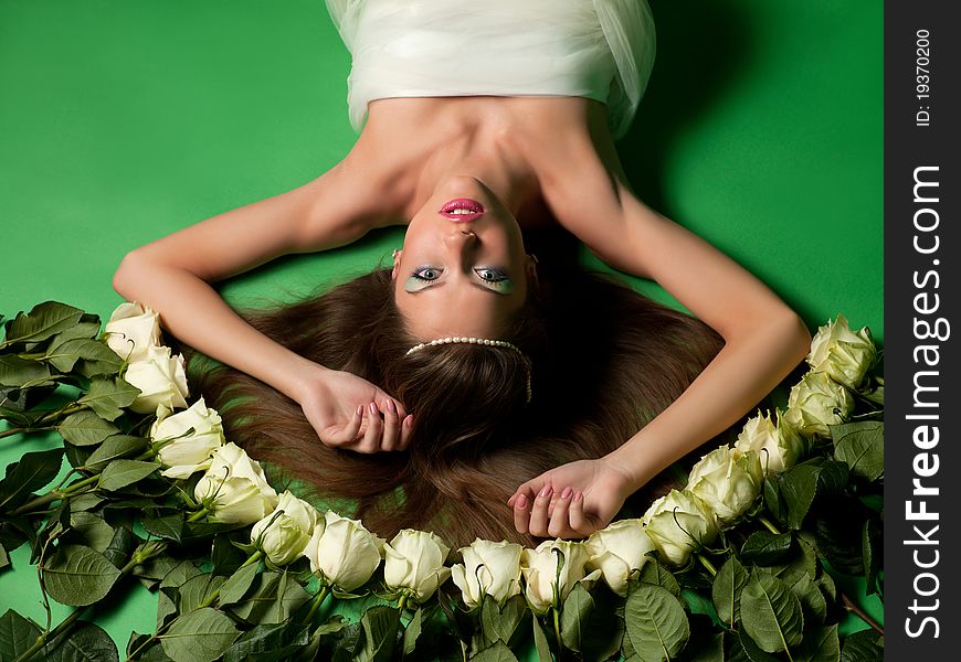 Young girl lay among the flowers of roses on a green background