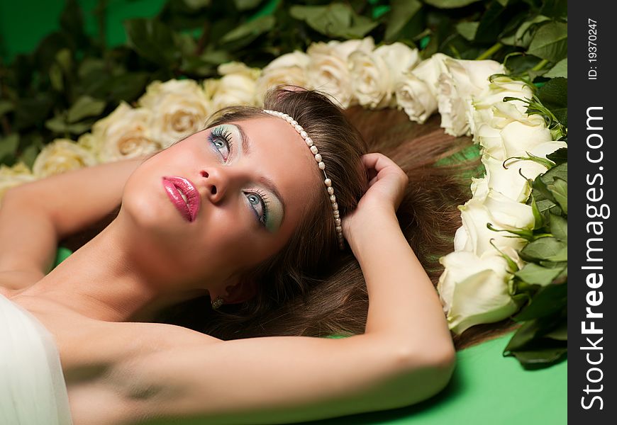 Young girl lay among the flowers of roses on a green background