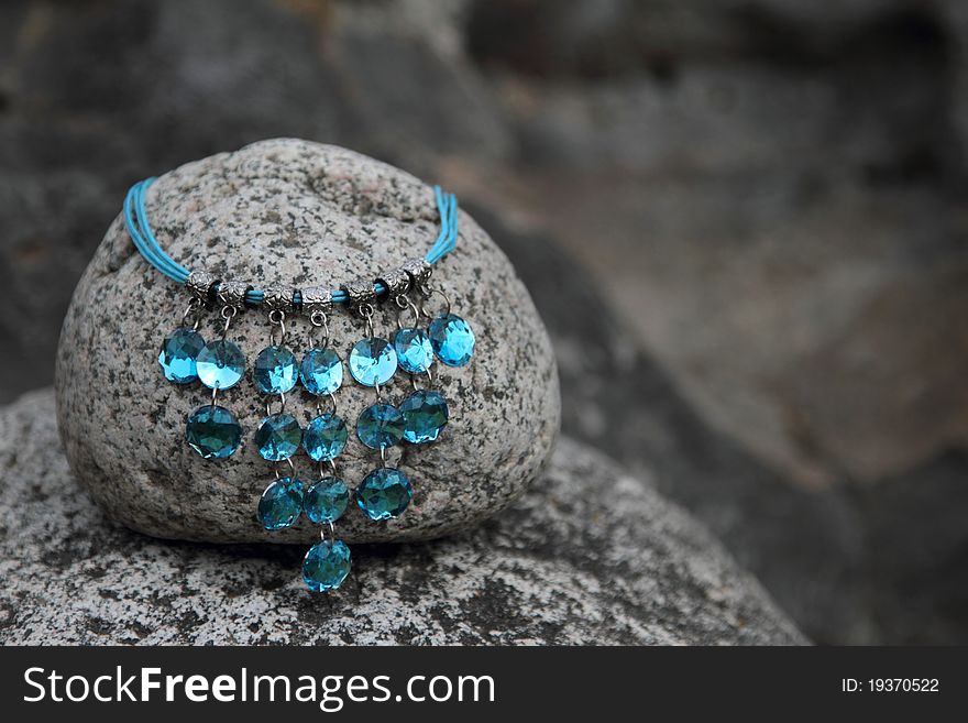 Blue gem necklace on a round grey rock. Blue gem necklace on a round grey rock