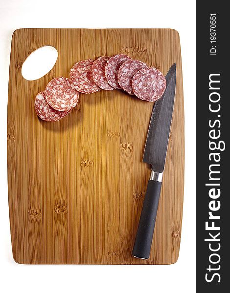 Sliced salami laying next to a knife on a brown cutting board. Sliced salami laying next to a knife on a brown cutting board.