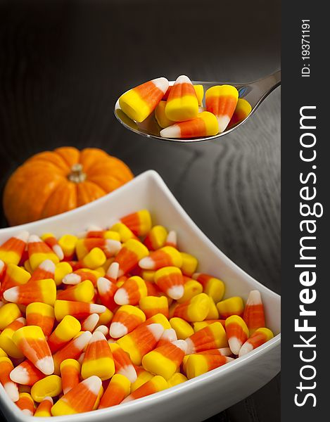 Spoon scooping candy corns out of a square dish. Spoon scooping candy corns out of a square dish