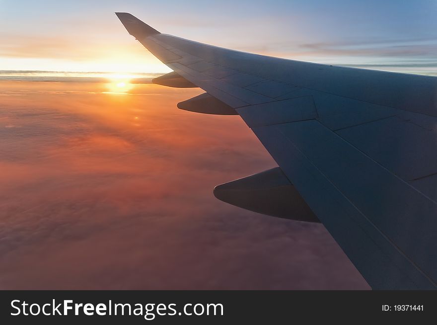 Airplane left wing on sunrise with a cloudy orange sky. Airplane left wing on sunrise with a cloudy orange sky