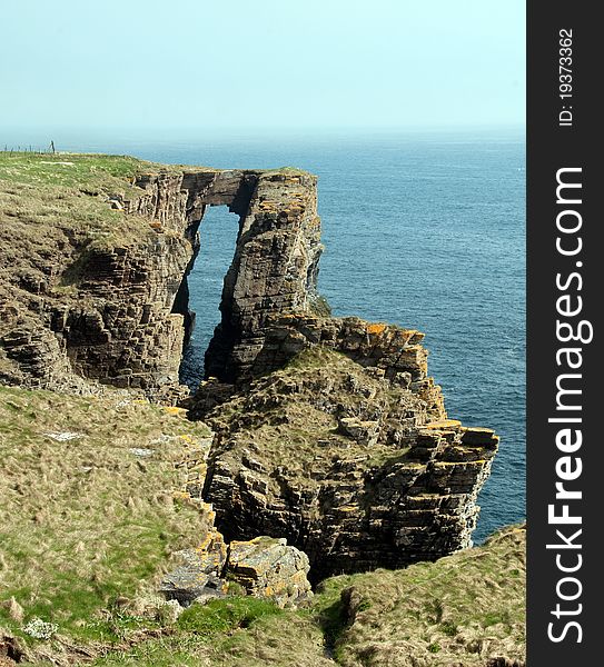 A Coastal Arch, near Wick. Caithness, Scotland, UK. The Arch is on the North east Coast of Scotland. This coastal arch called the Brig O Trams lies 5.6km south of Wick, Caithness, far North East Scotland, UK, Europe. The North sea has eroded and shaped this part of the cliff into a natural arch and bridge. The roof will collapse in time to form a free-standing stone stack. Caithness and North Coast Sutherland is a large area of unspoilt, dramatic scenery in the far north of Scotland, indeed, on the extreme edge of Europe. The borders of Caithness are the Pentland Firth to the north and Moray Firth to the east.