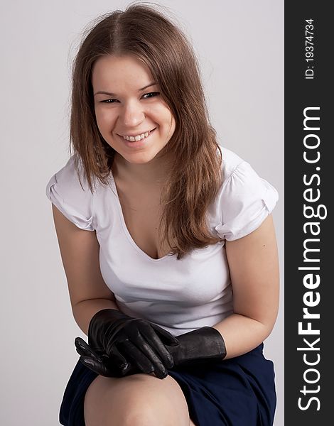 A girl sits in a light shirt and black gloves on a light background