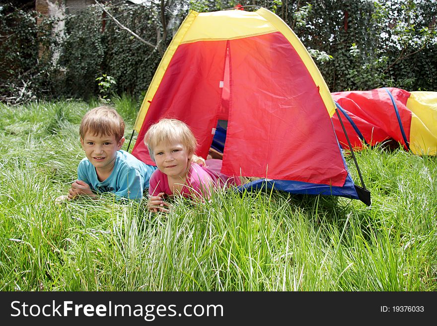 Young brother and sister laying near colorful tent on green grass on summer day. Young brother and sister laying near colorful tent on green grass on summer day